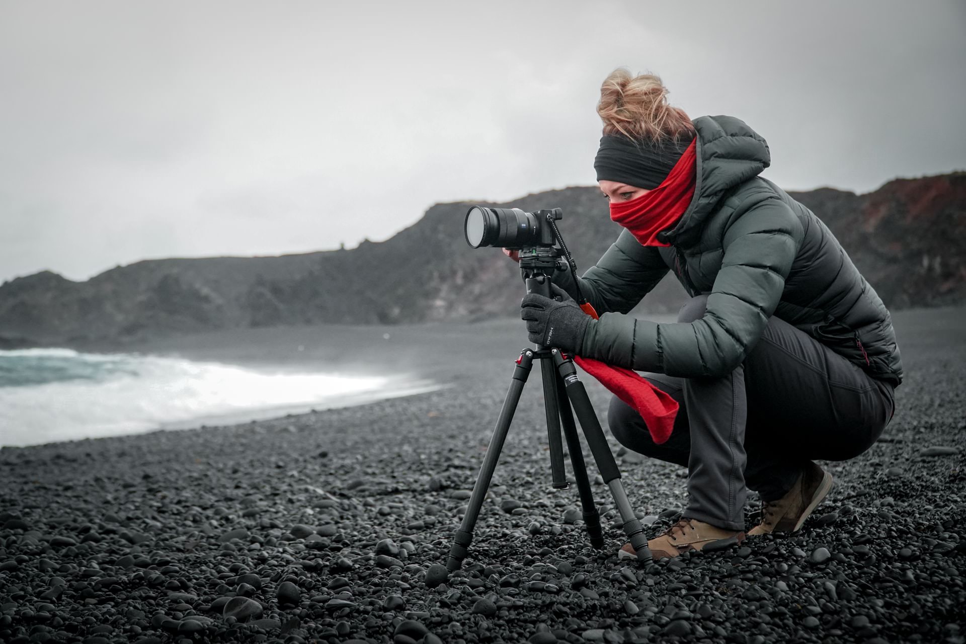 Woman with camera and tripod on a black sand beach.