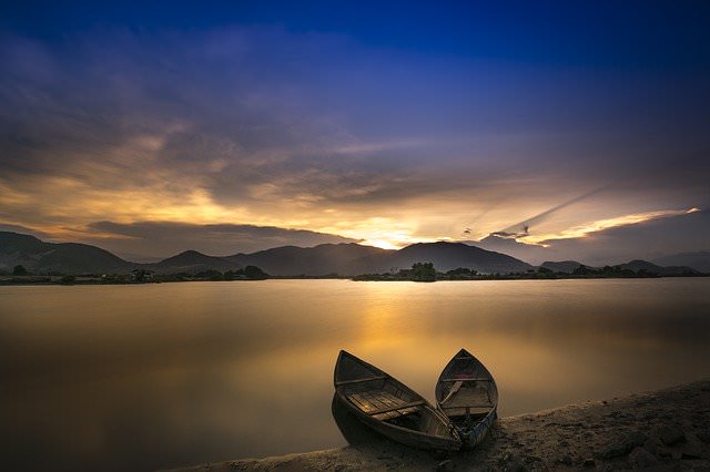 2 wooden boats in foreground with lake, mountains and sunrise in background