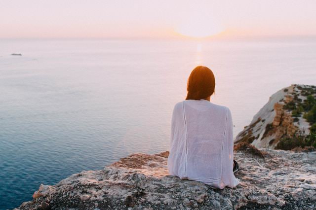 woman watching ocean and sunset from cliff