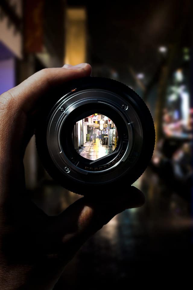 person holding camera lens with aperture viewable