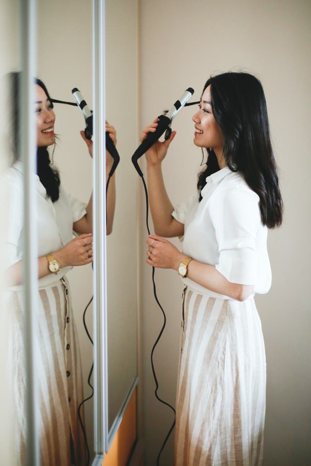 woman using curling iron in front of mirror