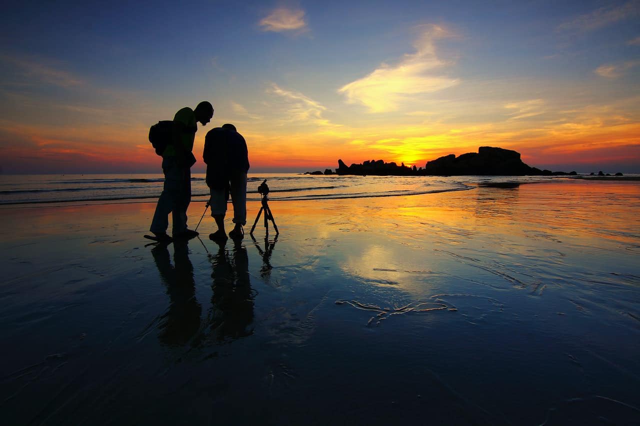2 personas fotografiando la puesta de sol con cámaras y trípodes