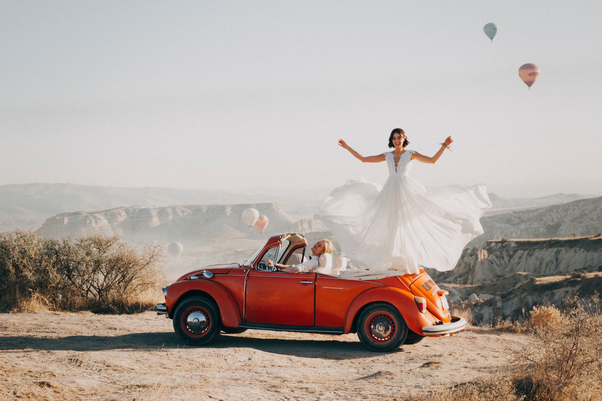 groom sitting in car while bride is standing on the car