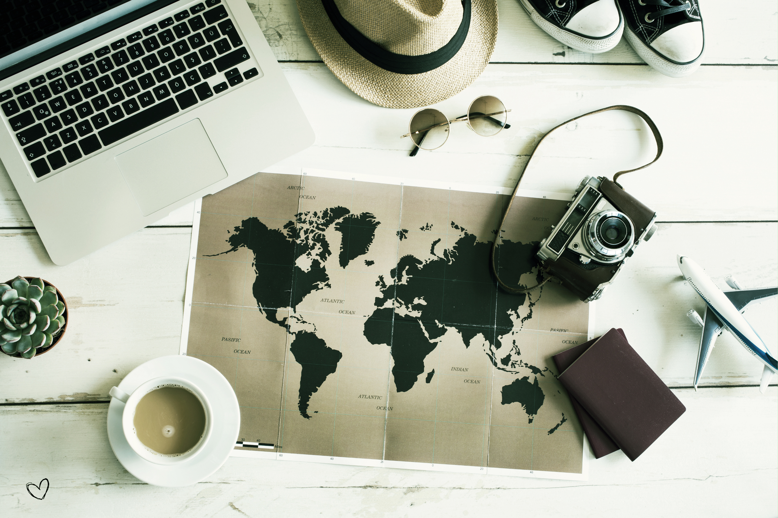 Laptop, coffee, world map, camera, and passports on a table.